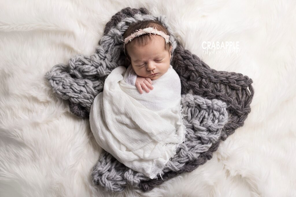 Swaddled newborn girl on white and gray chunky knit heart prop with matching headband.