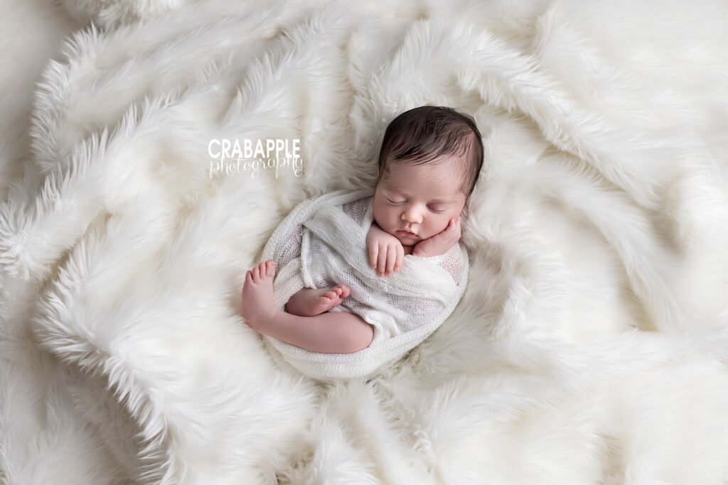 Peaceful newborn in soft white wrap on fluffy background by New England baby photographer
