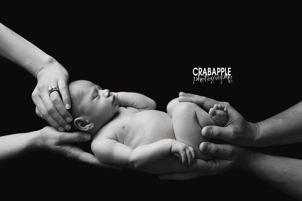 Black and white newborn photo with baby held by parents' hands — artistic family portrait.