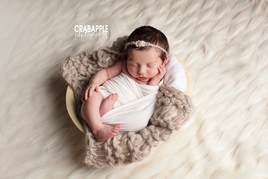 Smiling baby wrapped in soft knit blanket on ivory rug 


