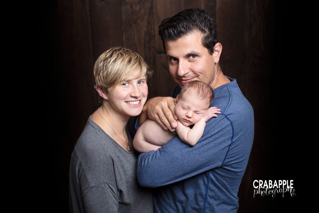 Parents holding newborn close during family photo session 

