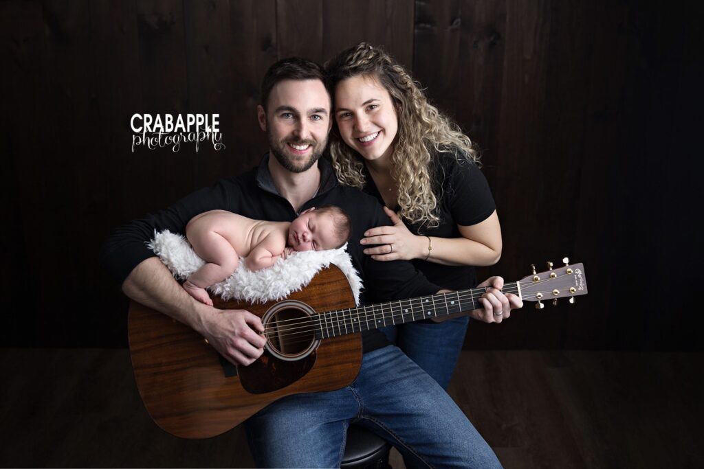 Family Newborn Portrait with Guitar Newborn baby resting on a guitar held by dad during a family portrait with mom and dad