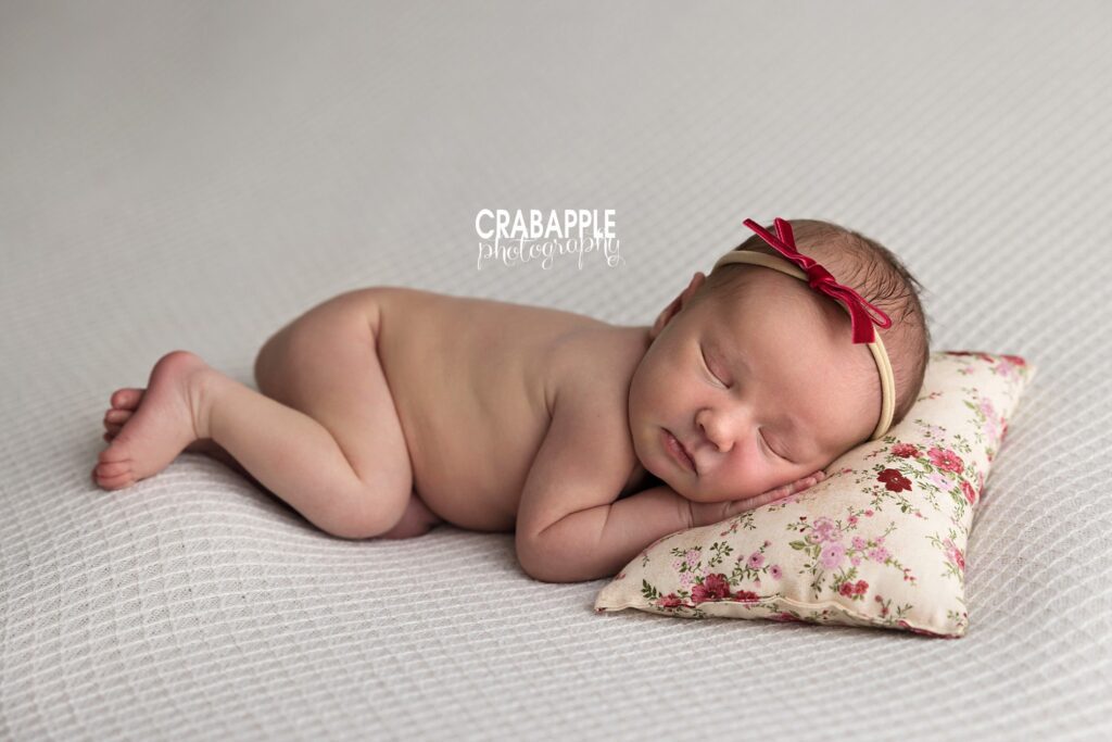Newborn baby girl sleeping with red bow headband on floral pillow – Boston baby photographer