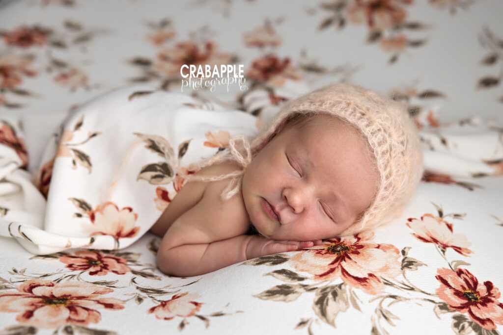 Newborn baby girl sleeping on floral blanket in knit bonnet  Massachusetts newborn photography
