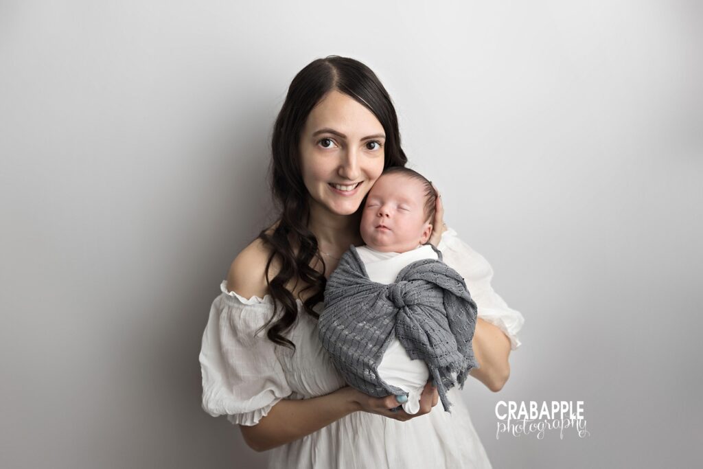 Smiling mother cradling newborn wrapped in gray
