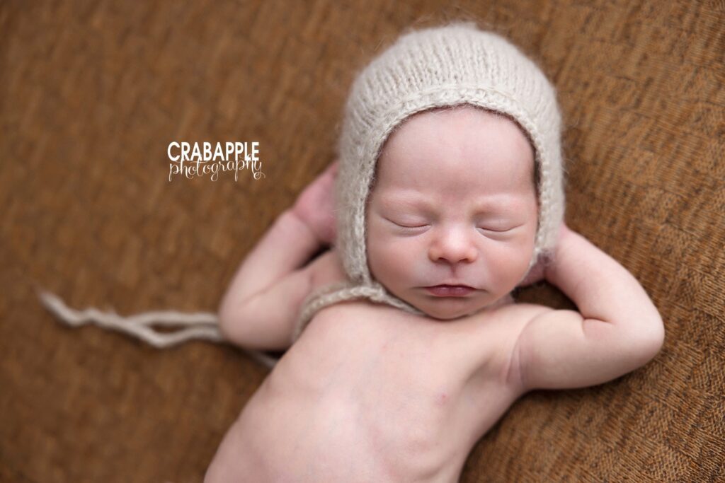 Newborn in tan knit bonnet with arms tucked behind head, classic baby photography pose Boston
