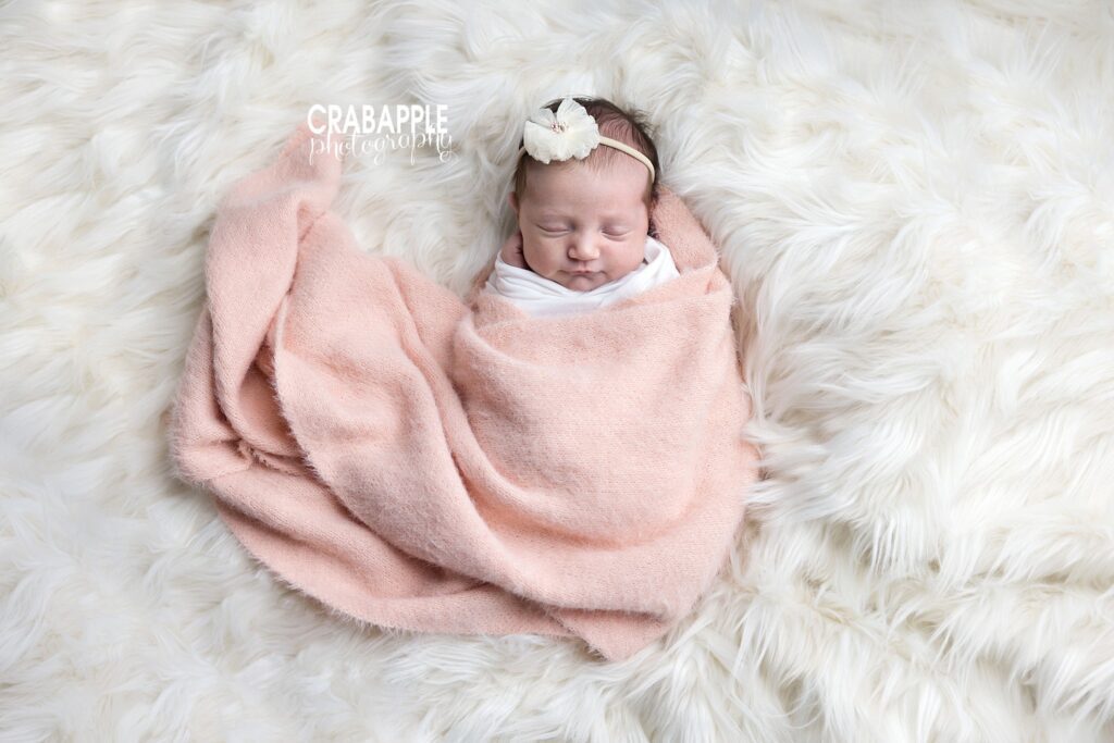 Swaddled newborn girl in pink blanket and bow on white fur – Boston baby photographer
