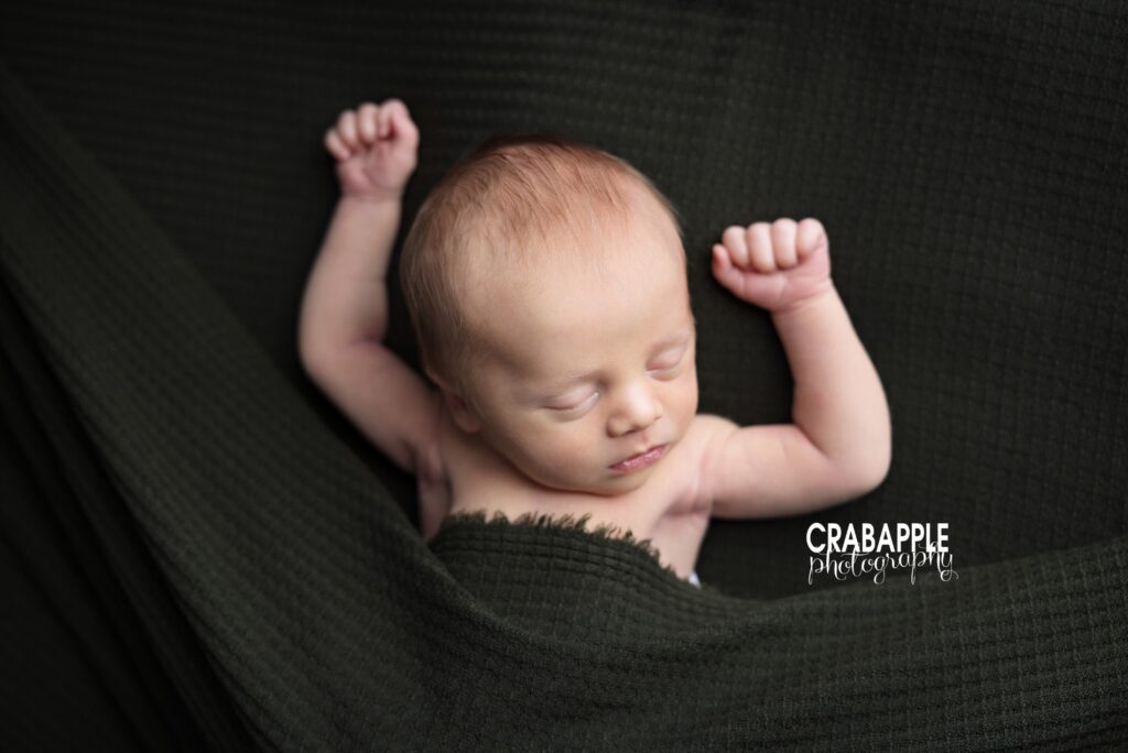 Baby posing on dark green textured blanket – creative Boston newborn photography

