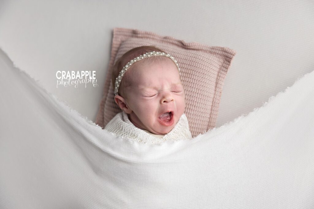 Yawning newborn swaddled in white blanket – candid baby photo Boston
