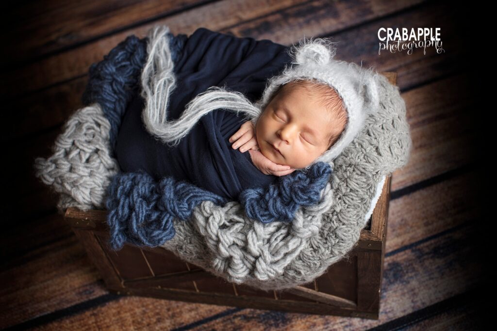 Newborn boy swaddled in blue and gray on wood backdrop 

