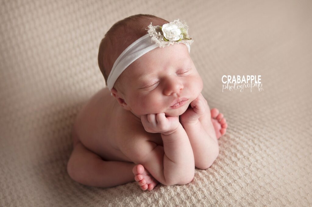 Close-up of newborn girl with flower headband resting chin on hands in the classic froggy pose

