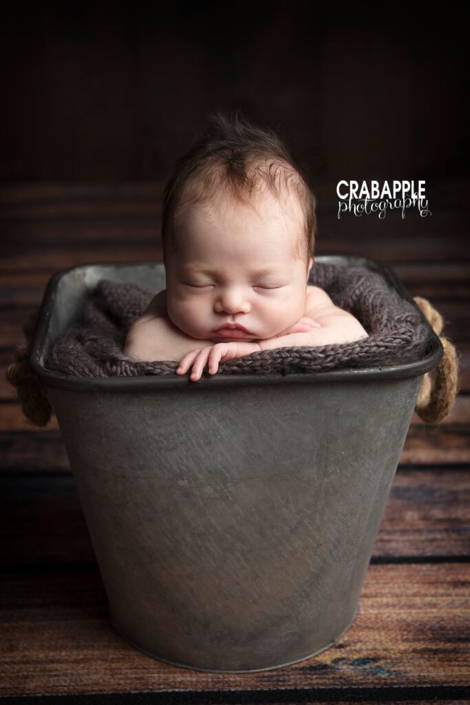 Baby resting arms on edge of metal bucket 