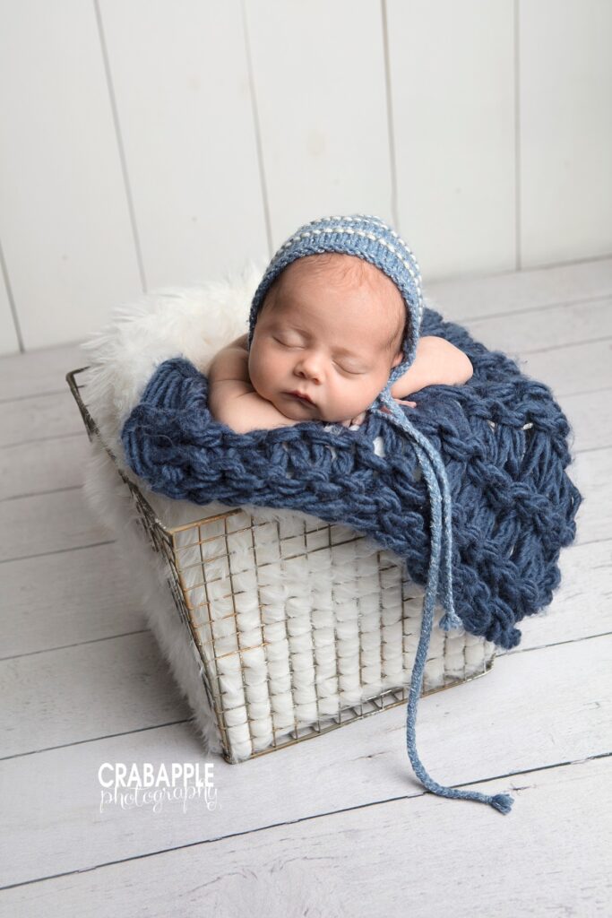 Newborn in blue bonnet sleeping in white basket 
