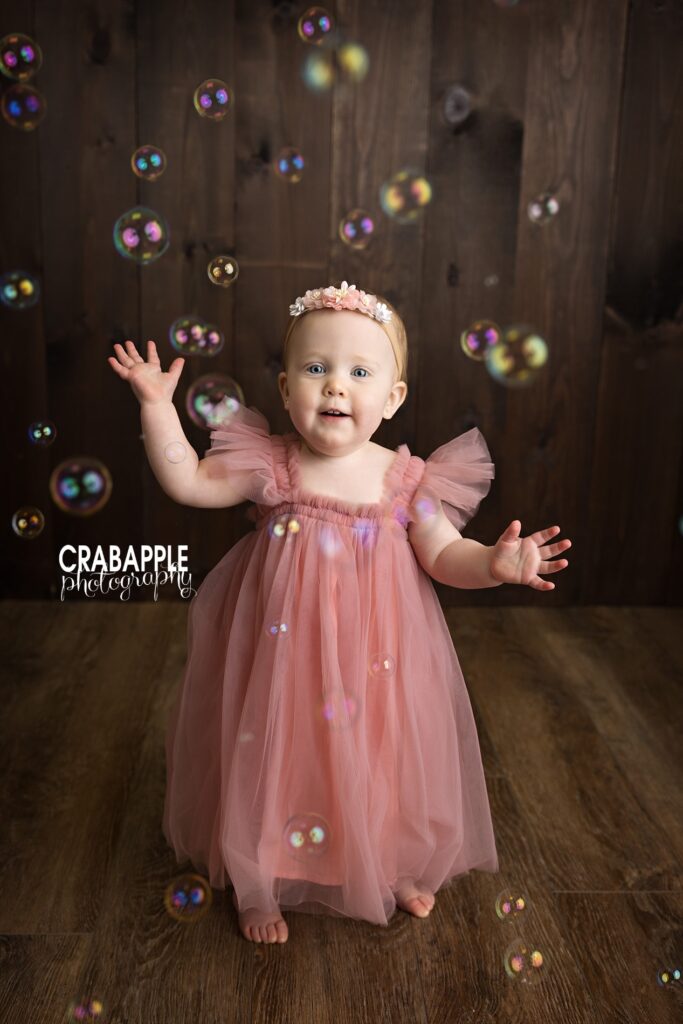 One-year-old baby standing and reaching for bubbles floating in the air.