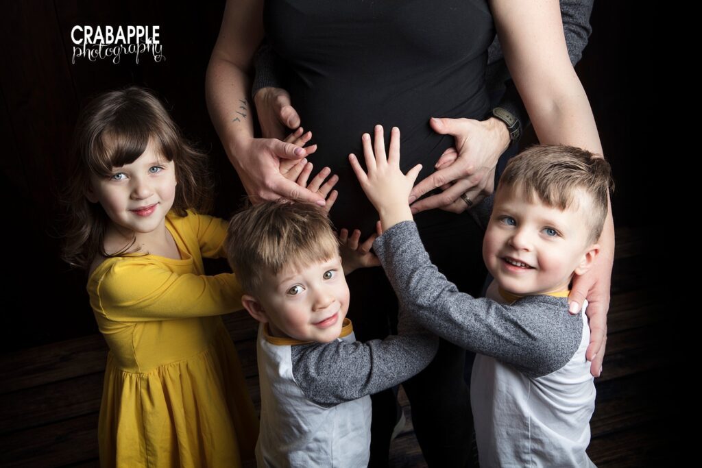 Close up portrait of three older siblings each placing their hands on mom's pregnant belly for a sentimental maternity portrait --maternity photographer boston