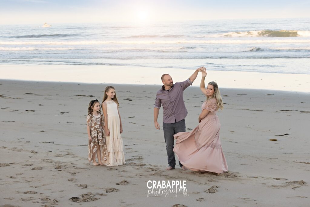 Parents dancing on the sand during beach photoshoot with children looking on