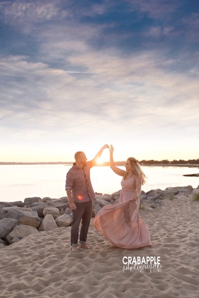 Couple spinning and laughing together near rocks during beach shoot