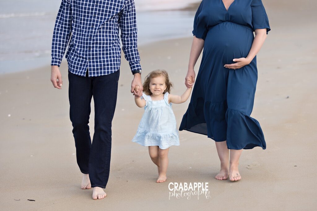 Maternity beach photos with toddler daughter near Boston Expecting mom and dad walking barefoot on the beach with their toddler daughter near Boston.