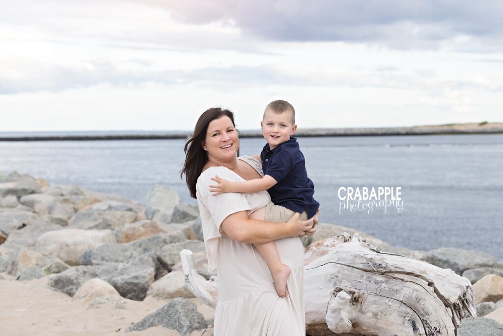 Pregnant mom holding toddler son on rocky beach during outdoor maternity session