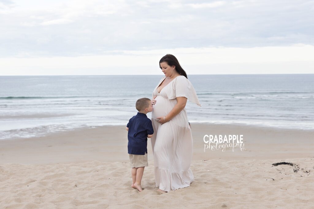 Boy kissing mom’s pregnant belly during beach photo shoot