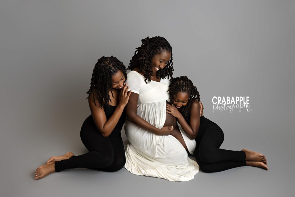 Studio maternity portrait of mom with two daughters resting heads on her belly