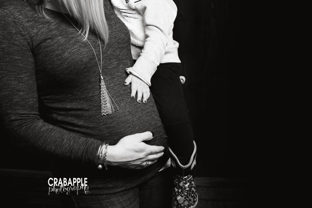 Black and white photo of mom holding toddler, with mom and sibling both resting a hand on the baby bump -- professional pregnancy photographer 