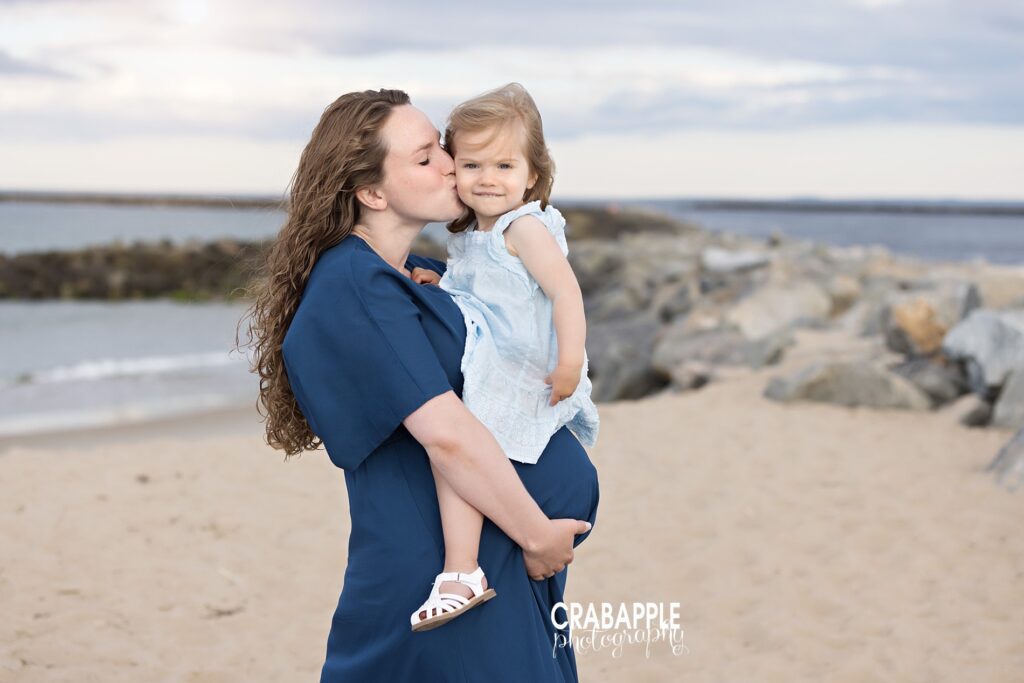 Mother and daughter maternity beach photo near Boston Expecting mom cuddling toddler daughter by the rocks at a Massachusetts beach.