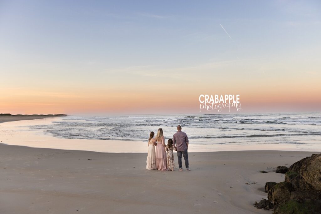 Family of four standing together at shoreline watching the waves during sunset