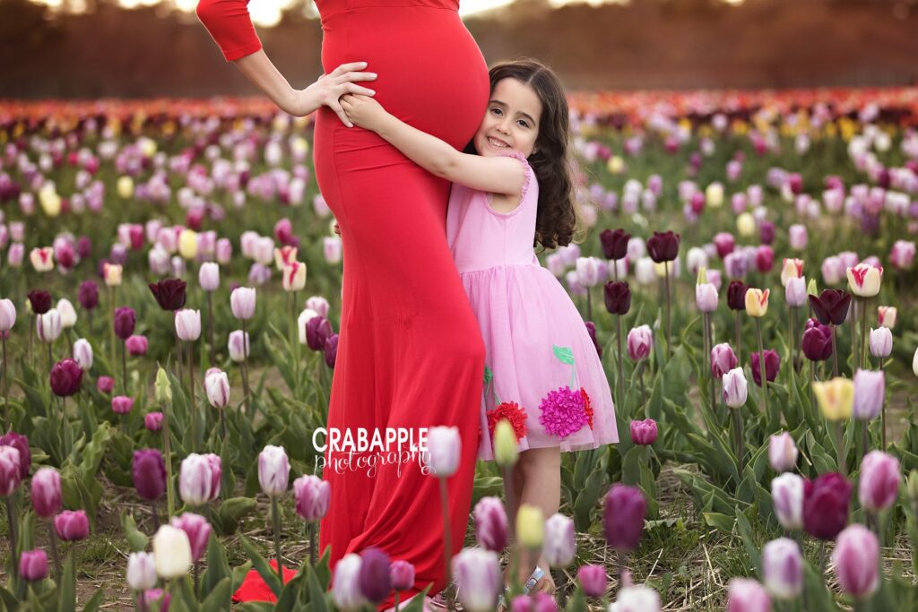 Girl hugging mom’s baby bump in a tulip field during spring maternity shoot -- professional pregnancy photographer 