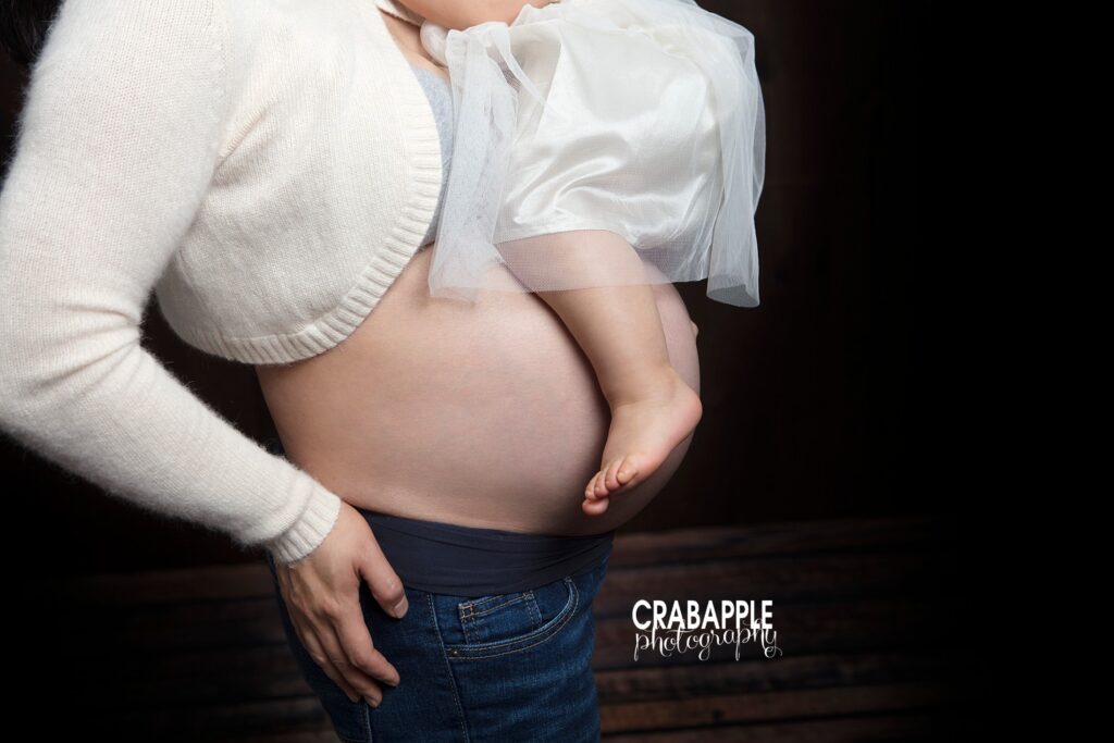 Toddler sitting on top of pregnant mother's exposed belly during maternity photo shoot
