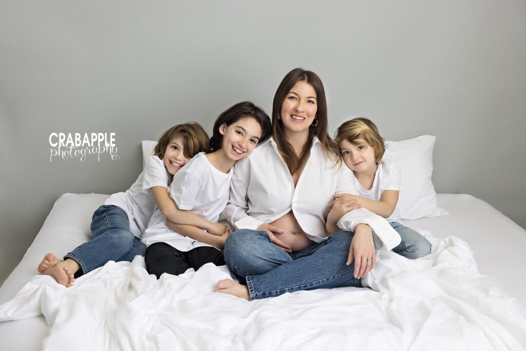 Mother sitting on bed with three young children during studio maternity session