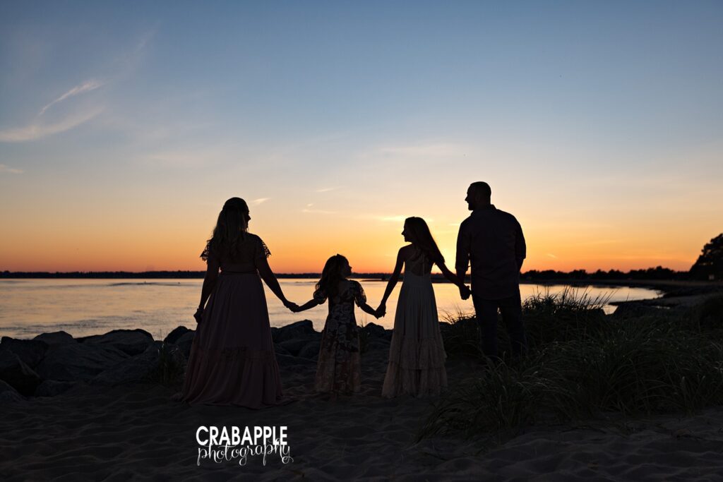 Family holding hands and walking along Salisbury Beach at sunset silhouetted