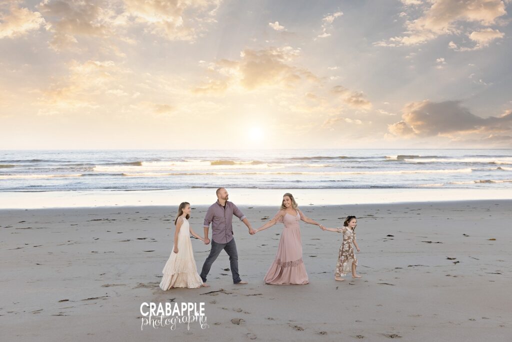 Family holding hands and walking toward ocean during golden hour