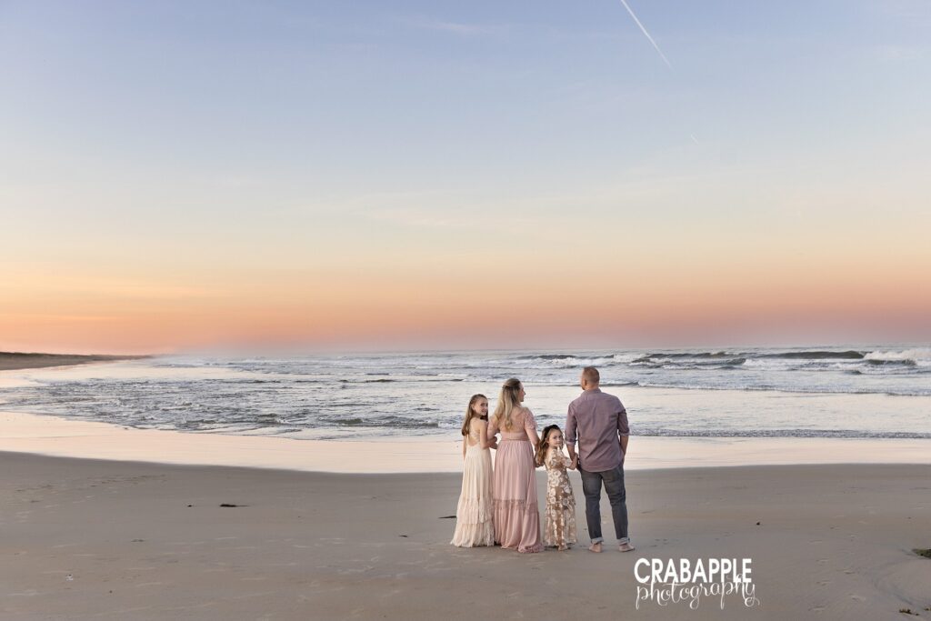 Family standing together on sandy beach at sunset with ocean backdrop