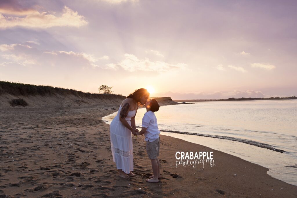 Silhouette beach portrait of mom and son kiss during Boston sunset Silhouette of mother kissing son as sun sets behind them at Boston beach