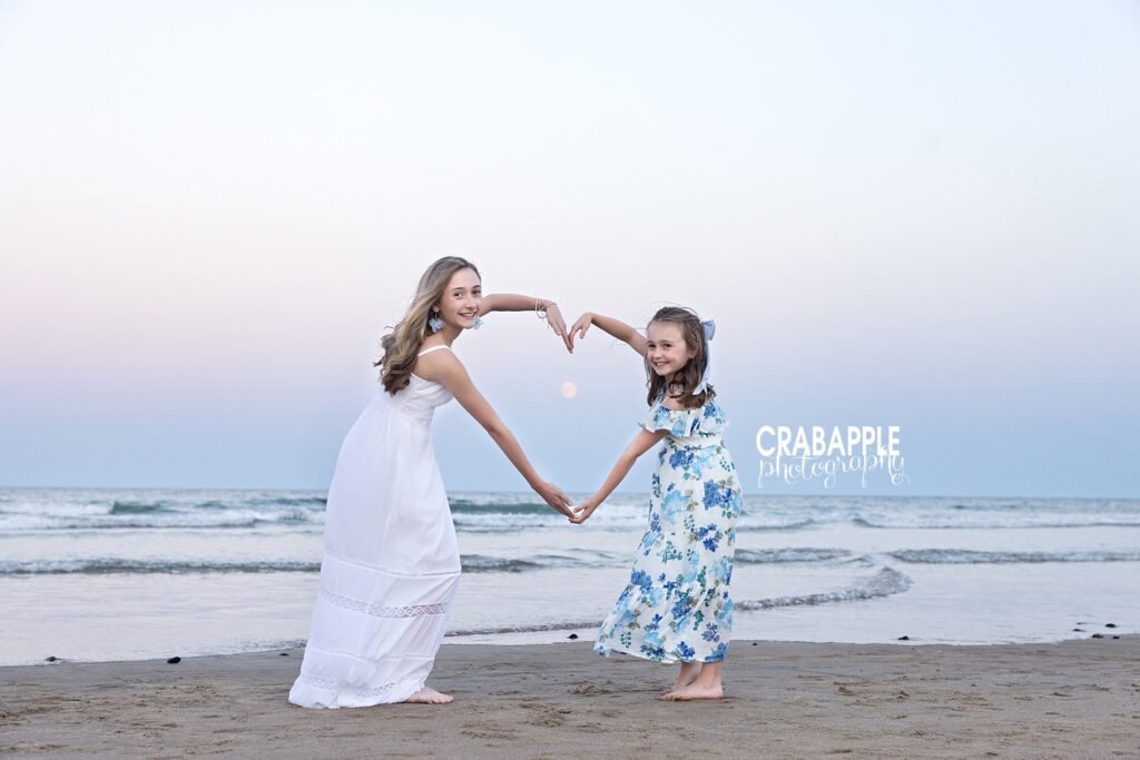 Whimsical ideas for sunset beach photos with children Sisters using arms to create a heart around a newly rising moon during sunset beach photos