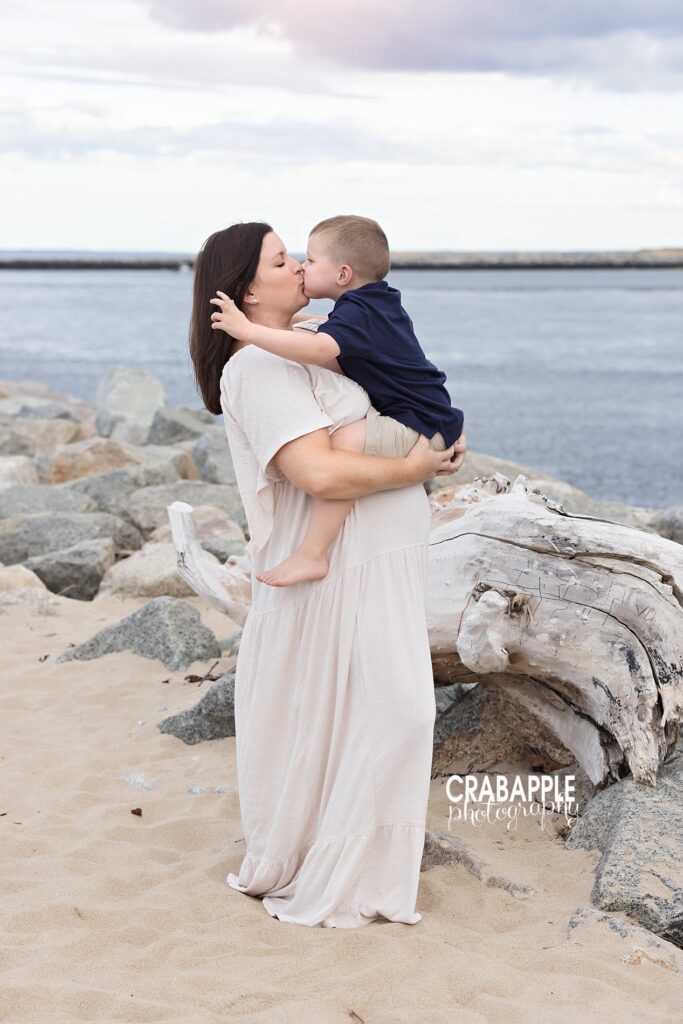 Pregnant mom holding and kissing toddler son during maternity beach photo session