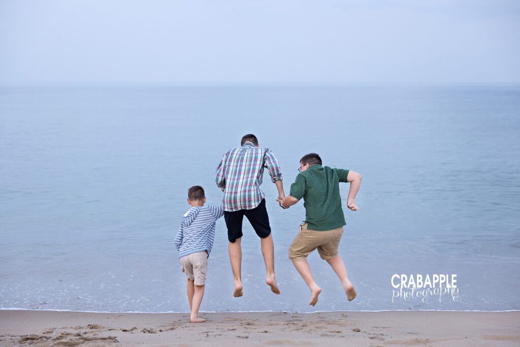 Three brothers jump over incoming waves during a family beach session near Boston