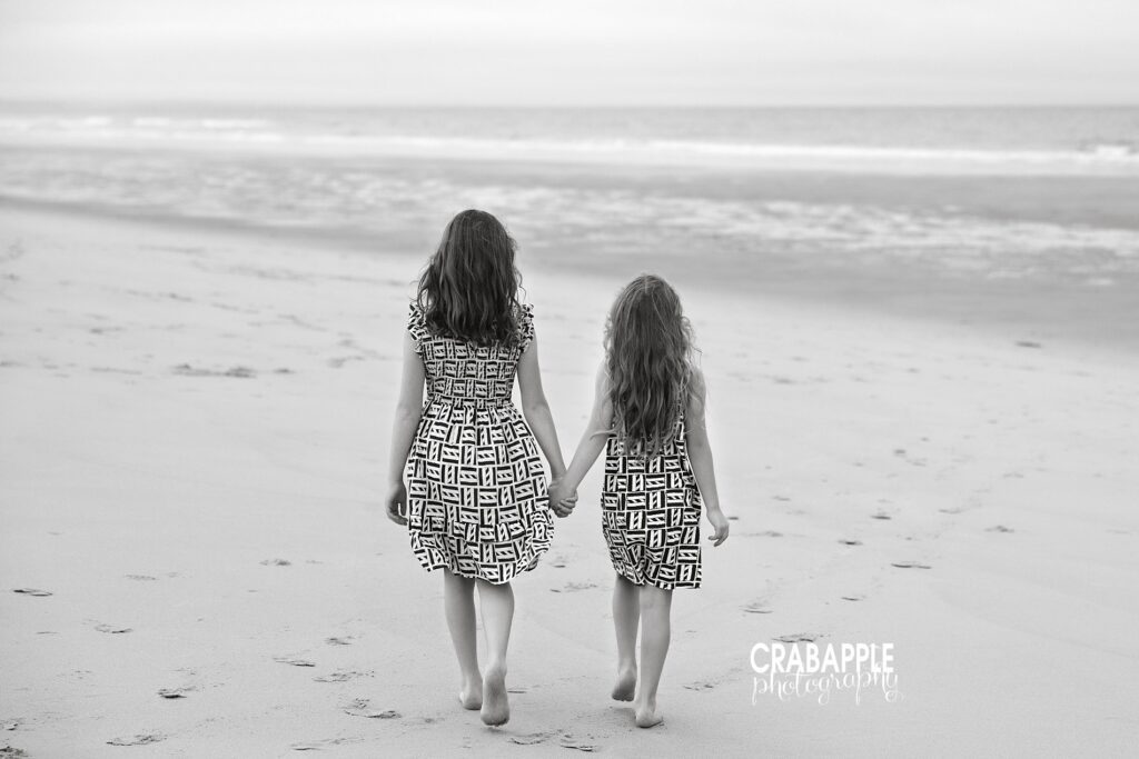 Black and white photo of two sistrs walking hand in hand along the sand