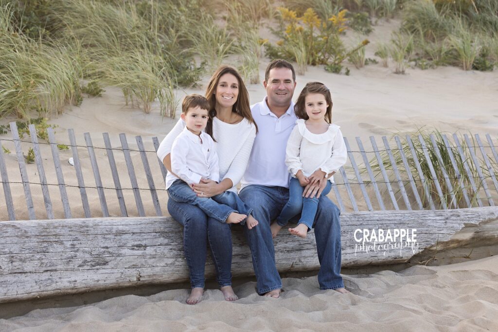 Boston area beach family photos Boston area beach family photos of mom, dad, and two toddler children sitting on a large piece of driftwood