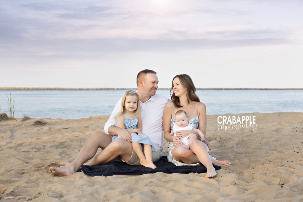Ideas for family beach photos Family photo of father, mother, and two daughters sitting on a beach blanket on the sand in front of the ocean