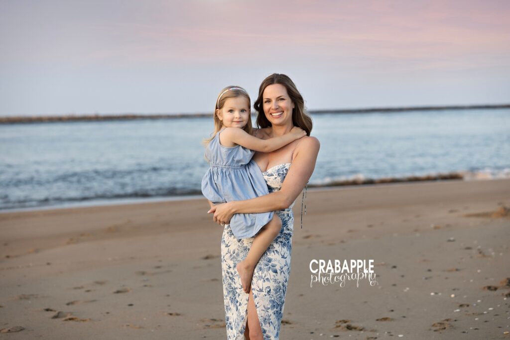 Sunset beach photos with mom and daughter Mother and daughter pose together in front of the ocean during a sunset beach portrait session