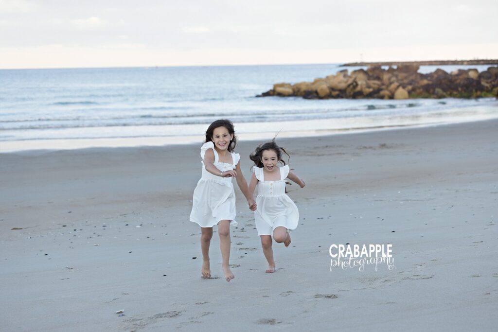 Candid photo of two sisters running along a sandy beach near Boston MA