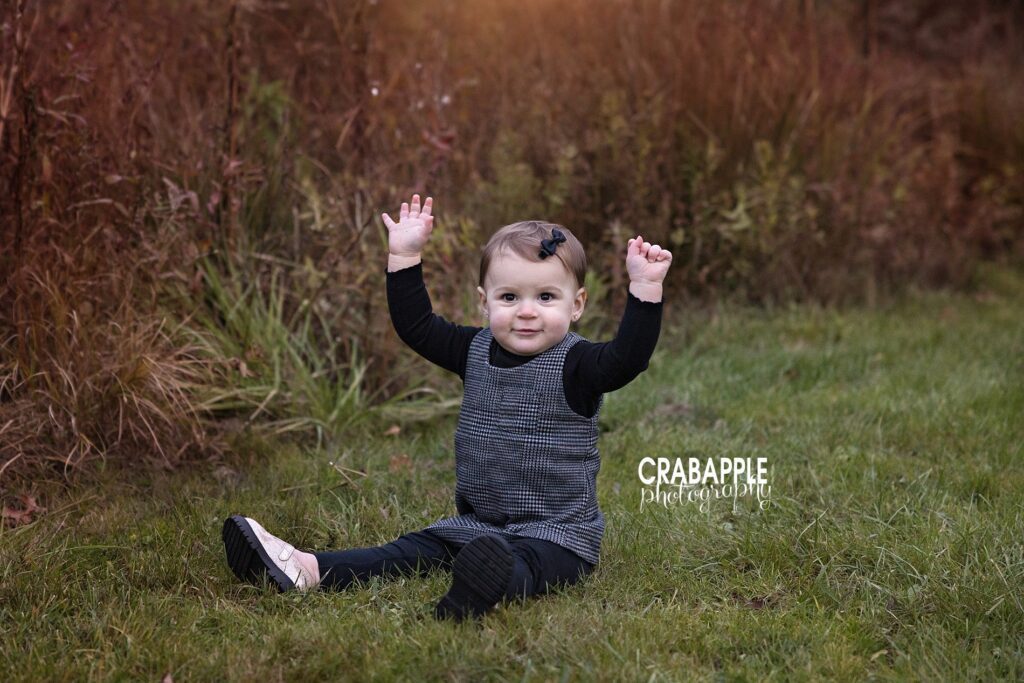 Outdoor baby photos in Massachusetts during fall One year old sitting on the ground surrounded by autumn colors and green grass