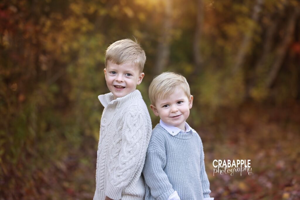 Two brothers standing back to back smiling at camera during fall family portraits in Lynnfield MA
