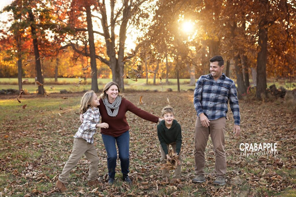 A fun and playful candid photo of a a family of four playing in the fall leaves outside near Somerville MA
