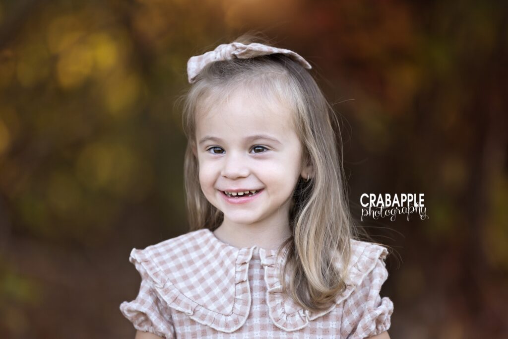 A young girl poses for fall portrait in a beige and cream gingham dress