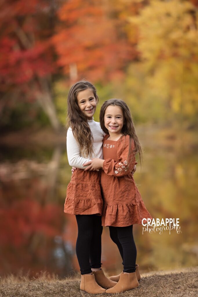 Two sisters pose for fall family photos in vibrant burnt orange coordinating outfits 