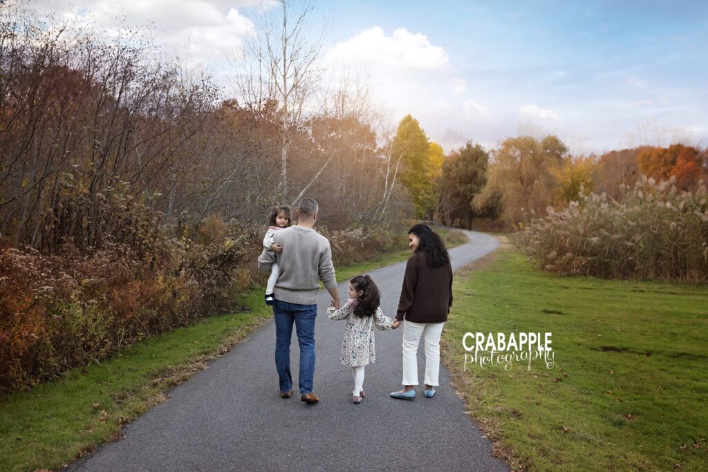 Family walking hand in hand during fall photos in Andover MA Family of four walking hand in hand outdoors during fall photos in Andover MA