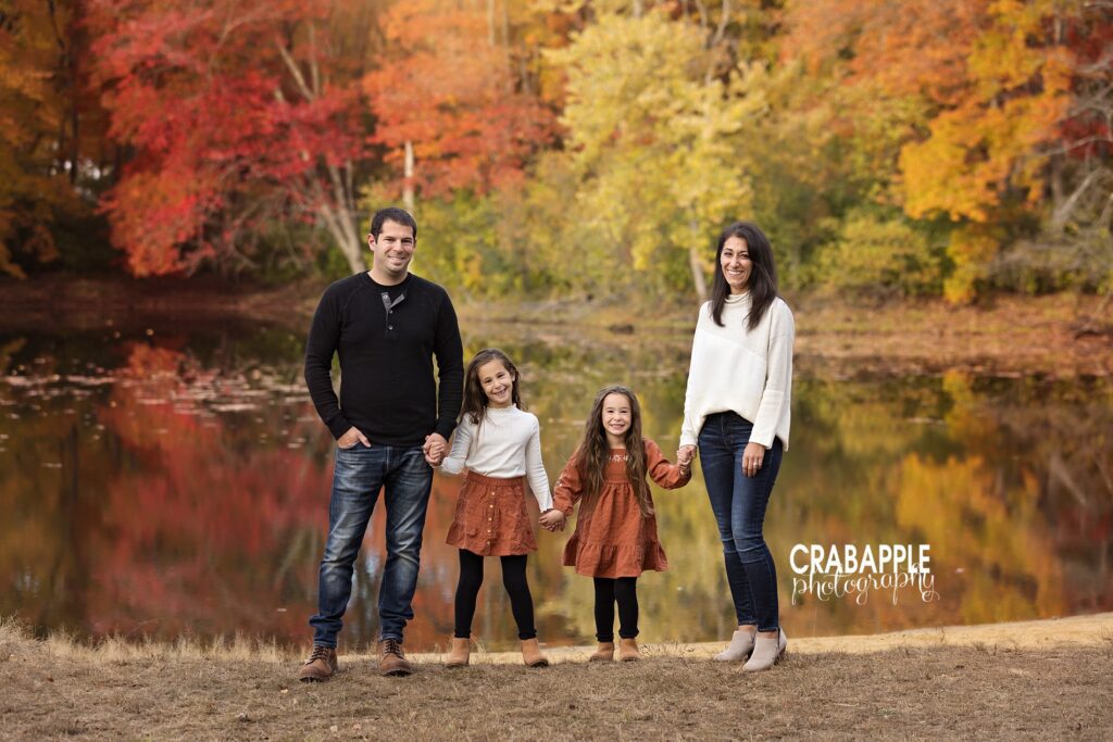 What to wear for fall family photos with colorful foliage backdrop Family of four standing together in coordinated fall family photo outfits surrounded by autumn foliage